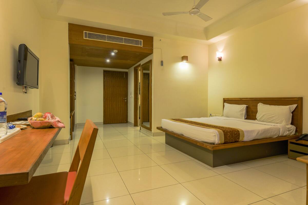 A hotel room with a bed, a desk, a chair, a television, and a ceiling fan.