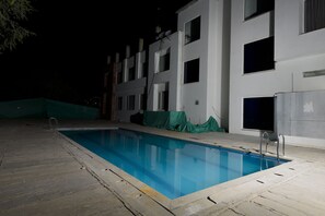 A swimming pool at night with a building in the background. - Shivam Resorts (Jaipur)