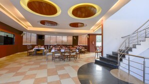 A spacious dining area with multiple tables and chairs, a staircase, and a modern ceiling design with circular light fixtures. - Shivam Resorts (Jaipur)