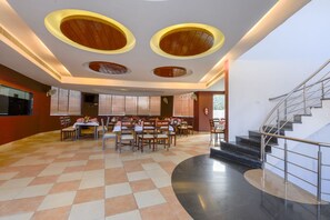 Un amplio comedor con varias mesas y sillas, una escalera y un diseño de techo moderno con lámparas circulares.