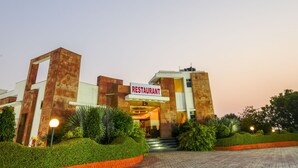 A modern restaurant building with a sign, surrounded by well-maintained hedges and a paved entrance area. - Shivam Resorts (Jaipur)