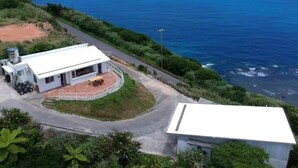 A coastal property with a white building, a paved road, and a view of the ocean. - Happy coral (Higashi)