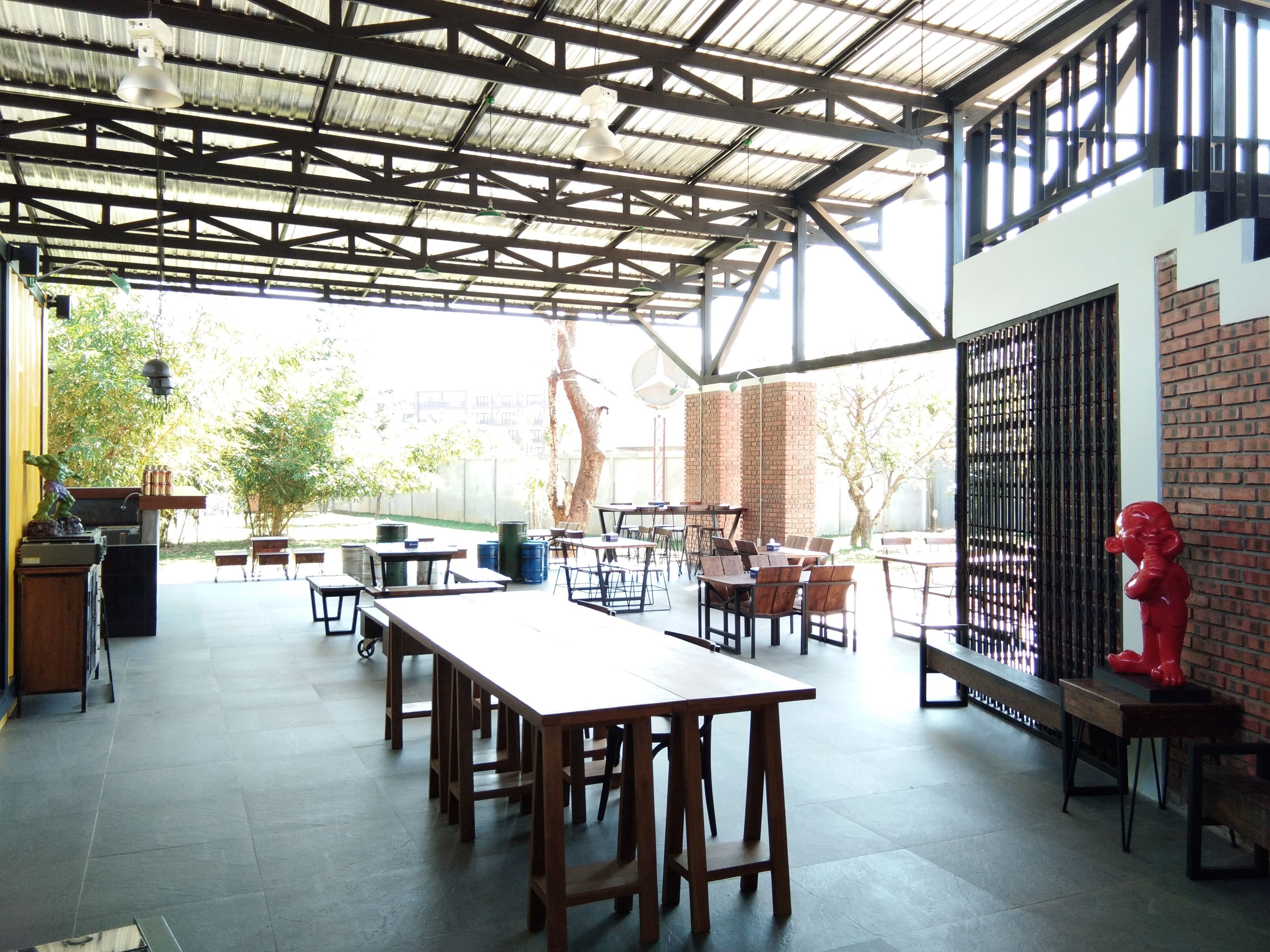 An outdoor dining area with multiple wooden tables and chairs, a brick wall, and a metal fence.