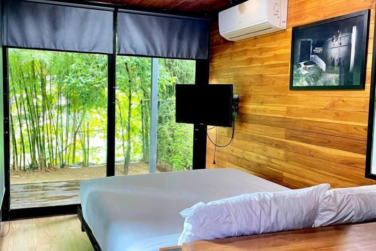A bedroom with a large window, a bed, a wall-mounted TV, and an air conditioning unit.