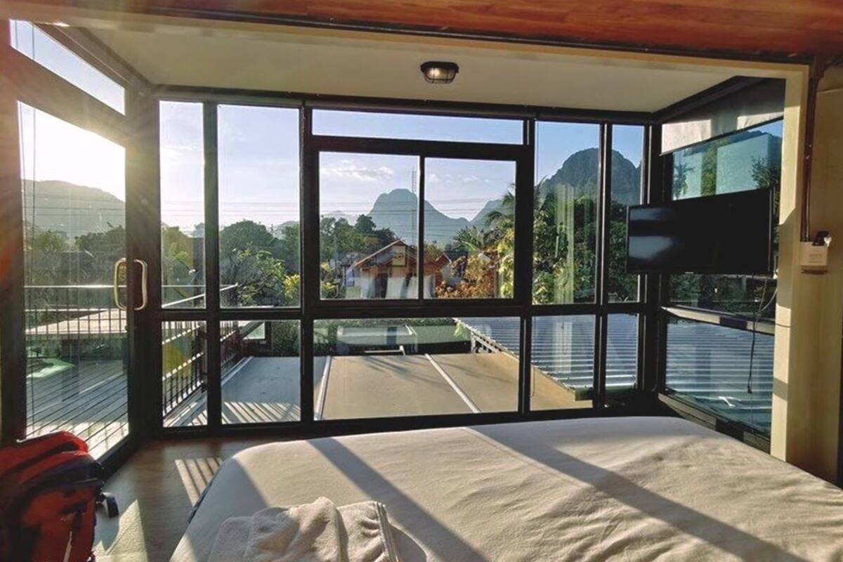Une chambre dotée d’un lit, d’une télévision et de grandes fenêtres donnant sur un paysage montagneux.