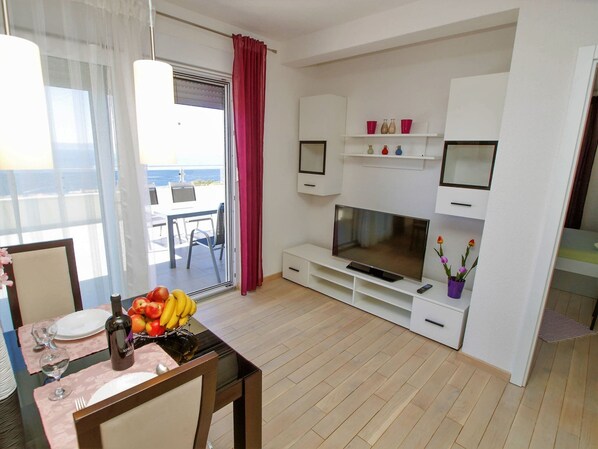 A modern living room with a flat-screen TV, white cabinets, a dining area with a table set for two, and a balcony with a table and chairs. - Adria View, Apartment Dino, Whirlpool, pool (Makarska)