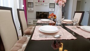 Een eethoek met een tafel gedekt voor vier personen, inclusief borden, bestek en glazen. Er staan stoelen rond de tafel en een vaas met bloemen op tafel.