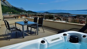 Een balkon met een jacuzzi, een tafel en stoelen, met uitzicht op een schilderachtig meer en bergen.
