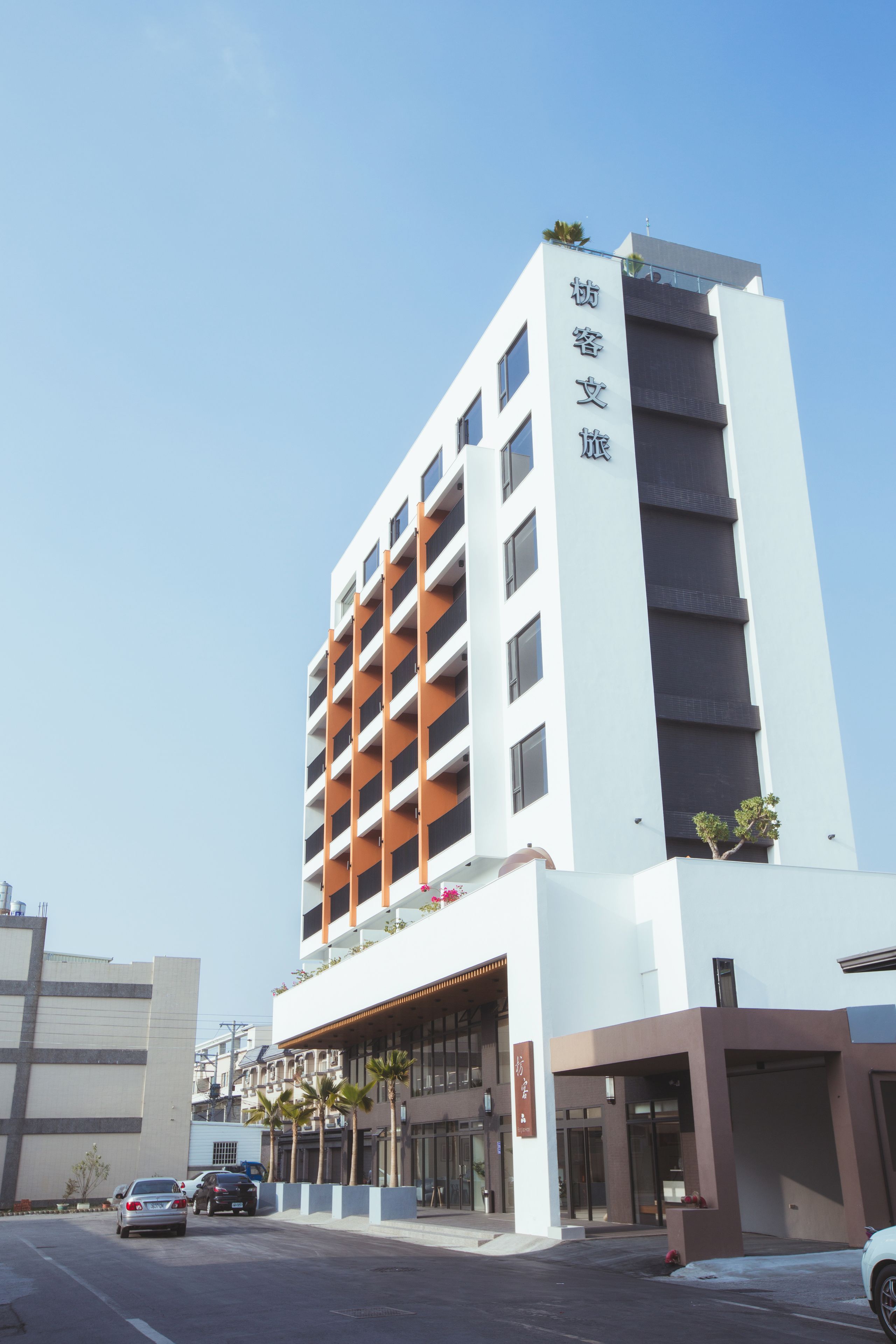 A modern hotel with a white facade, multiple balconies, and a clear sky.