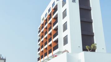 A modern hotel with a white facade, multiple balconies, and a clear sky.
