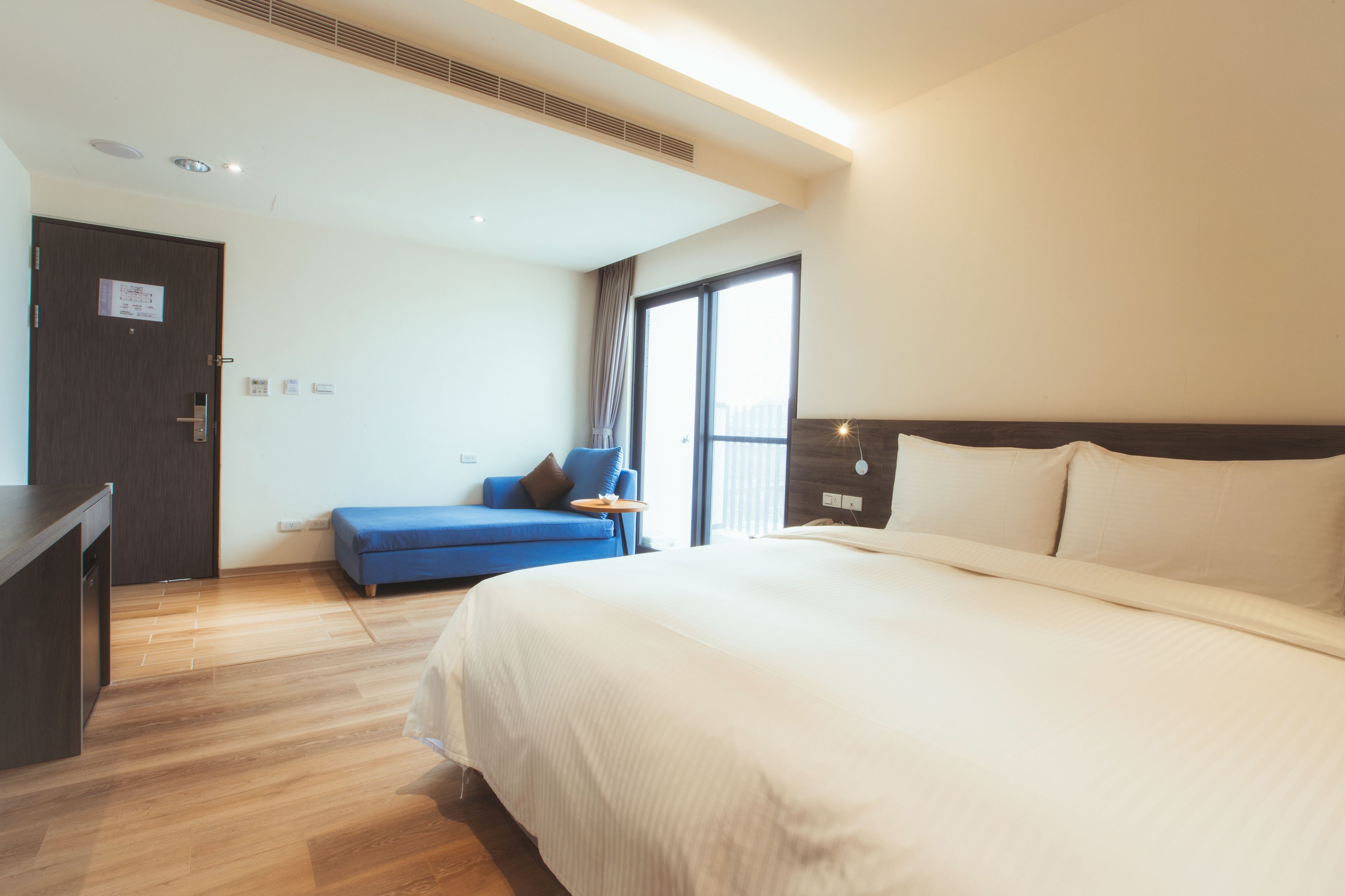A hotel room with a large bed, a blue sofa, a small table, and a door with a sign.