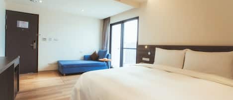 A hotel room with a large bed, a blue sofa, a small table, and a door with a sign.