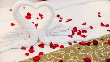 Una cama con sábanas blancas y una disposición decorativa de toallas en forma de cisne, junto con pétalos de rosa esparcidos.