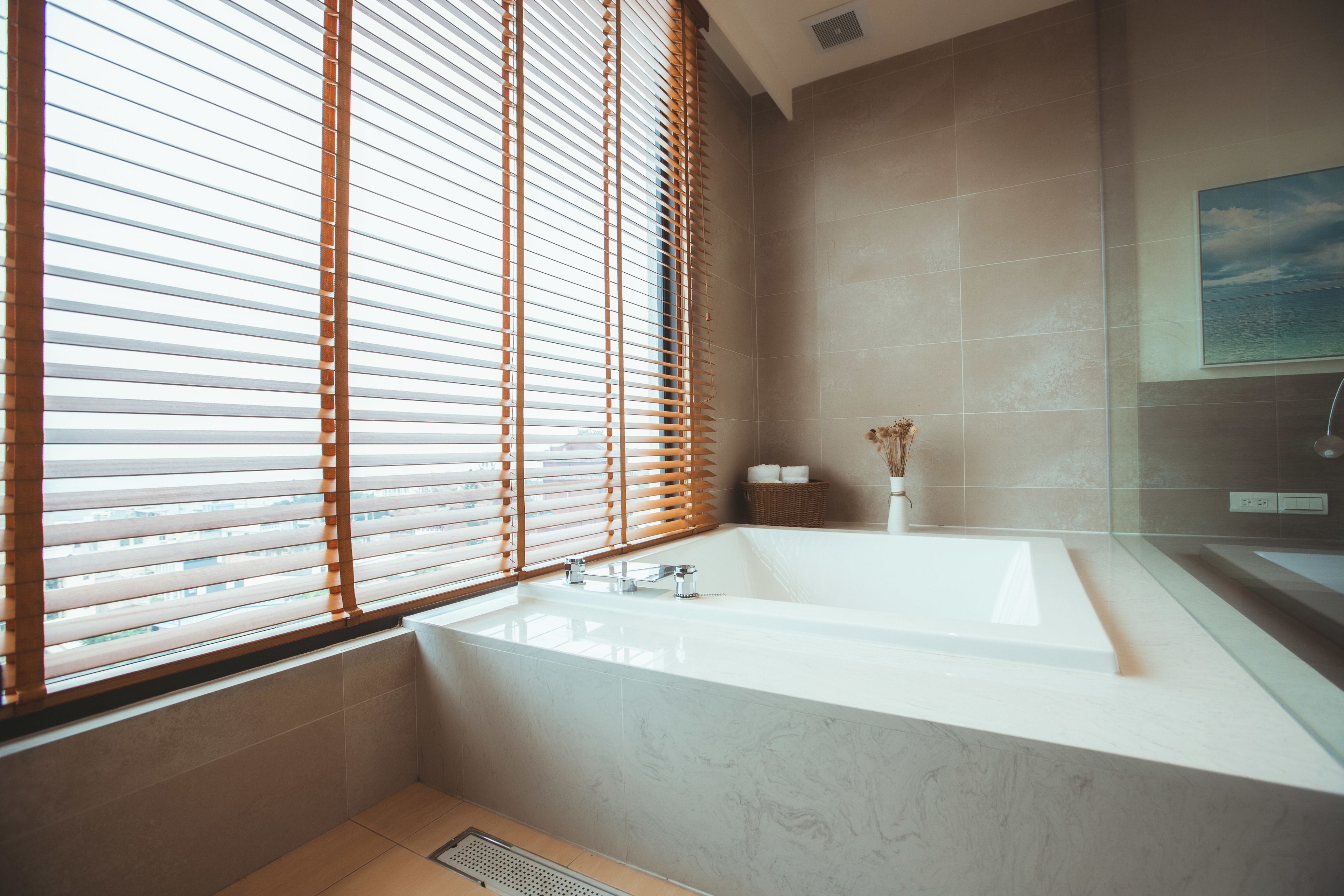 Un baño moderno con una bañera grande, persianas de madera y vista al mar a través de la ventana.