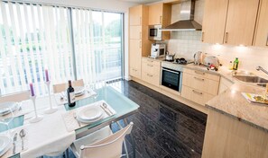A modern kitchen with a dining area, featuring a large window, a built-in oven, and a microwave. - Exclusive apartment with water view - Apartment Meierwik (Glücksburg (Ostsee))