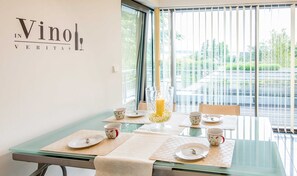 Ruokailutila, jossa on neljälle katettu pöytä, kynttilöistä koostuva koriste ja suuret ikkunat, joista avautuu näkymä parkkipaikalle.