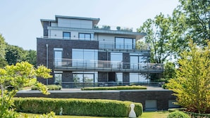 A modern multi-story building with large windows and balconies, surrounded by well-maintained gardens and trees. - Exclusive apartment with water view - Apartment Meierwik (Glücksburg (Ostsee))