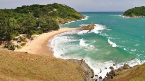 A coastal landscape with a beach, rocky shoreline, and lush greenery. - Porterhouse Beach Hotel (Patong)