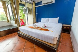 A hotel room with a bed, curtains, an air conditioning unit, and a view of greenery outside. - Porterhouse Beach Hotel (Patong)