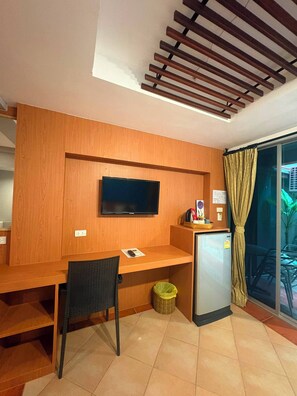 A hotel room with a wooden desk, a television mounted on the wall, a small refrigerator, and a chair. - Porterhouse Beach Hotel (Patong)