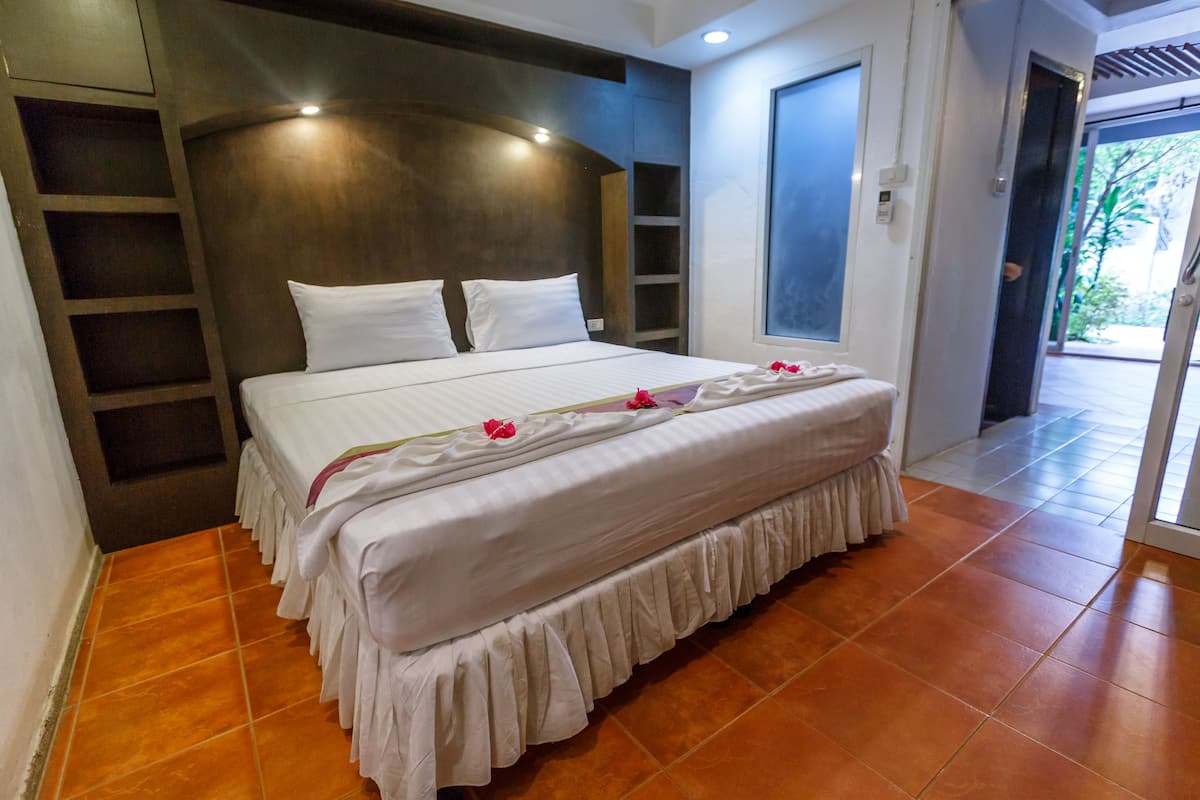 A bedroom with a large bed, a wooden headboard, and a view of the outdoors through a glass door.