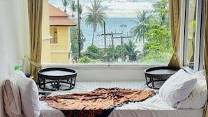 A room with a bed, two small tables, a view of the sea, and a tiled floor. - Porterhouse Beach Hotel (Patong)