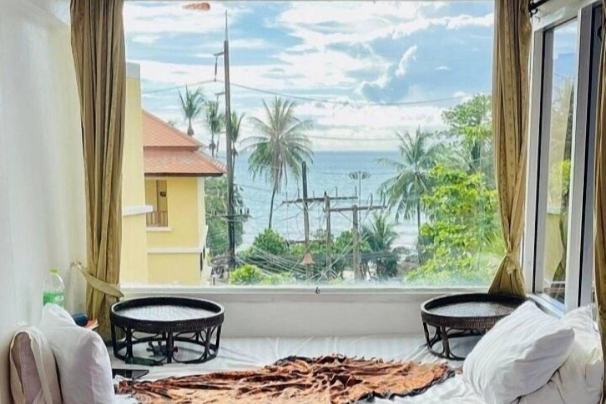 A room with a bed, two small tables, a view of the sea, and a tiled floor.