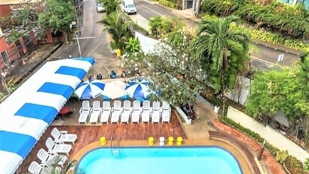 A pool area with lounge chairs and umbrellas, surrounded by greenery and buildings. - Porterhouse Beach Hotel (Patong)
