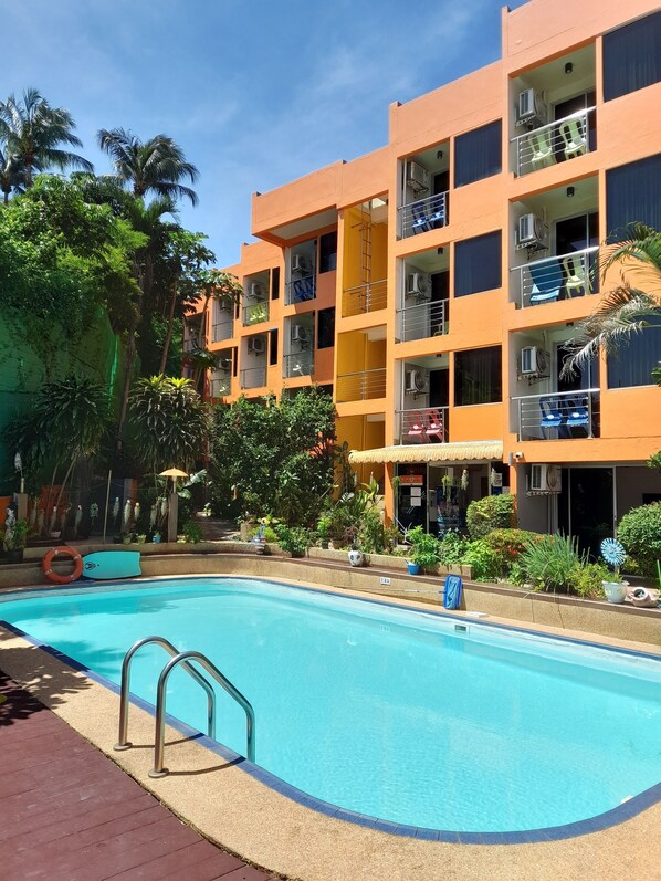 A multi-story building with balconies, a swimming pool, and surrounding greenery. - Porterhouse Beach Hotel (Patong)