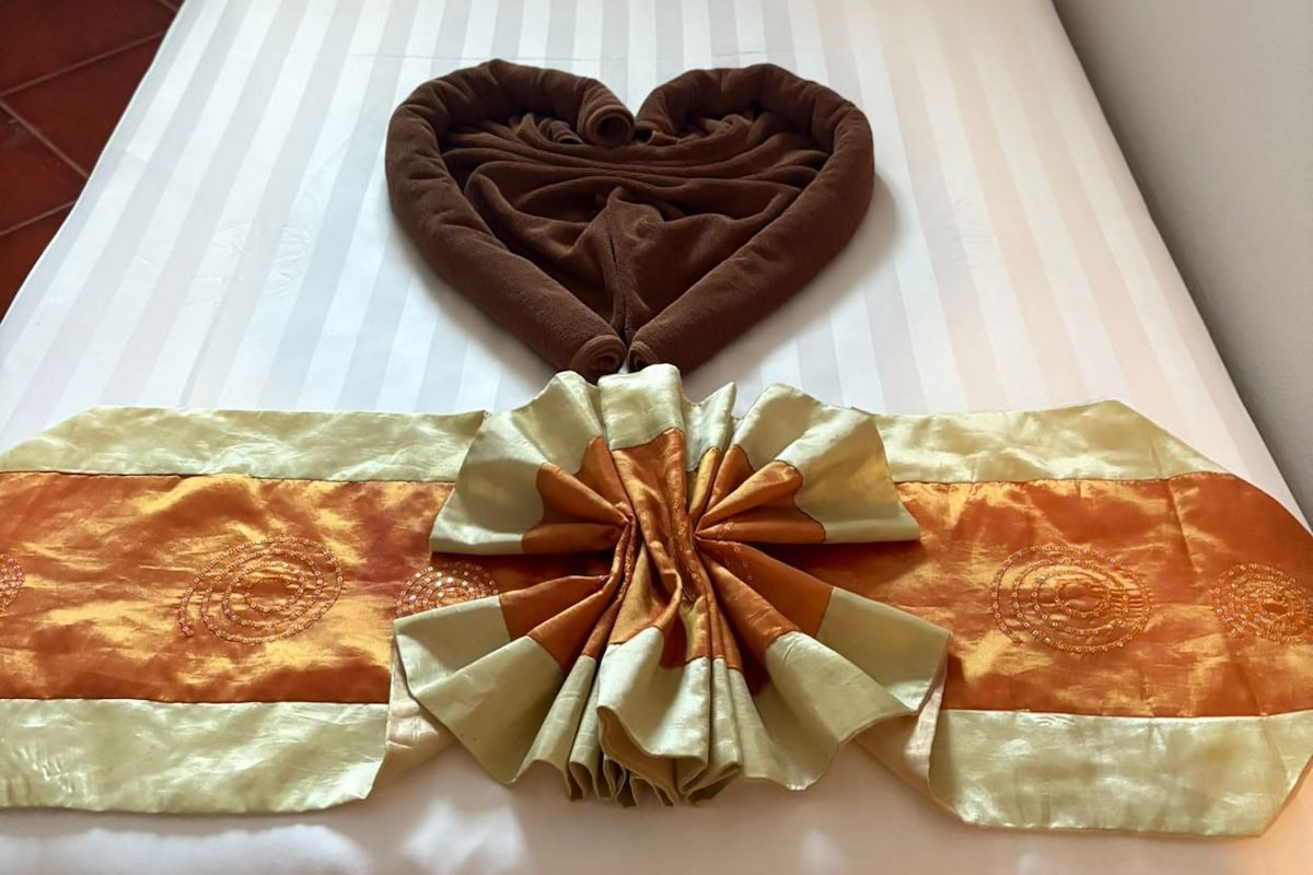 Cama bem arrumada com travesseiro em formato de coração e um laço decorativo na colcha.