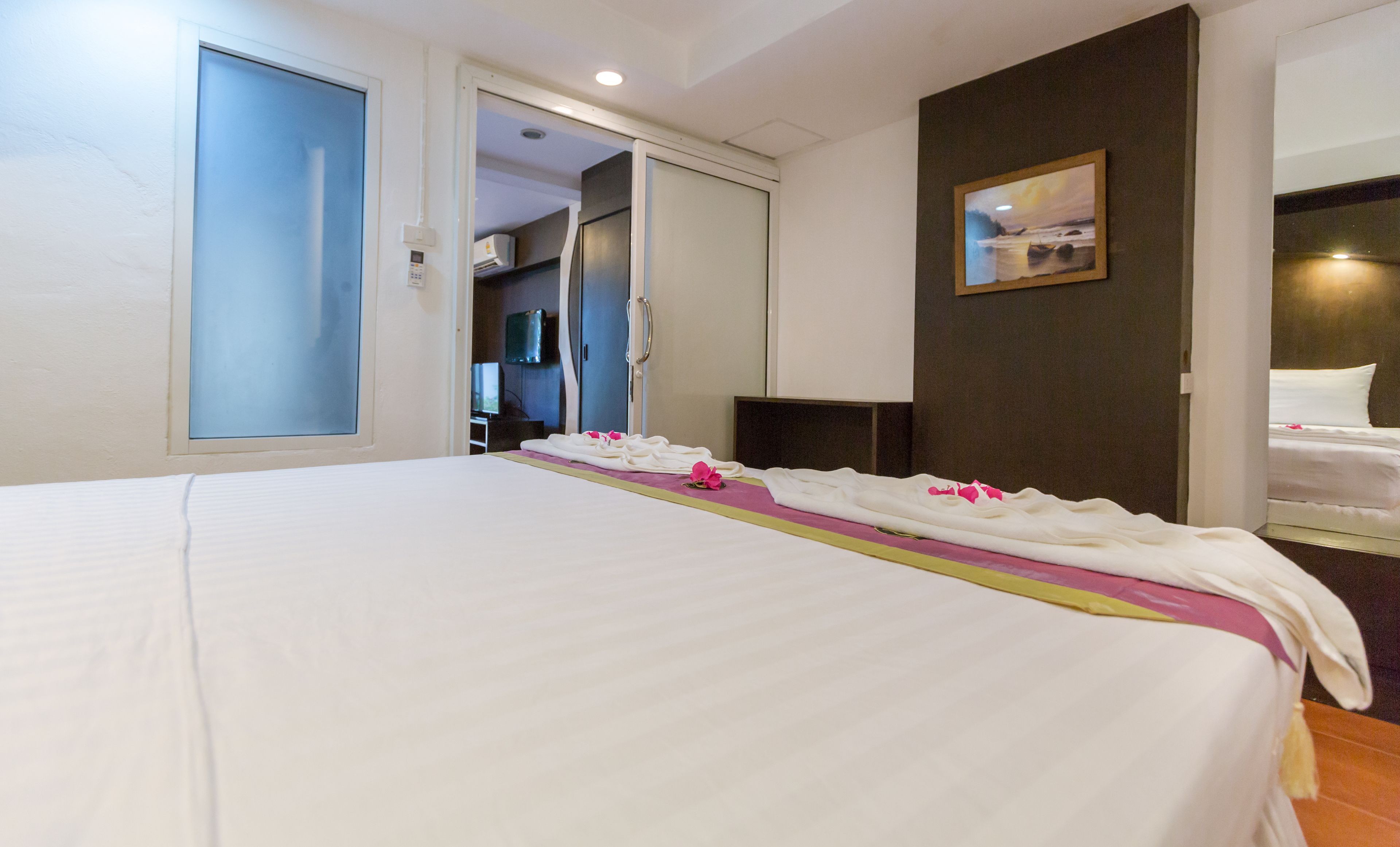 A hotel room with a large bed, a bedside table, a mirror, and a painting on the wall.