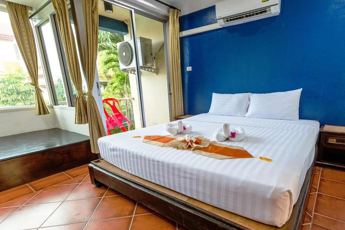 Quarto de hotel com cama, janela com cortinas, aparelho de ar condicionado e uma cadeira vermelha.