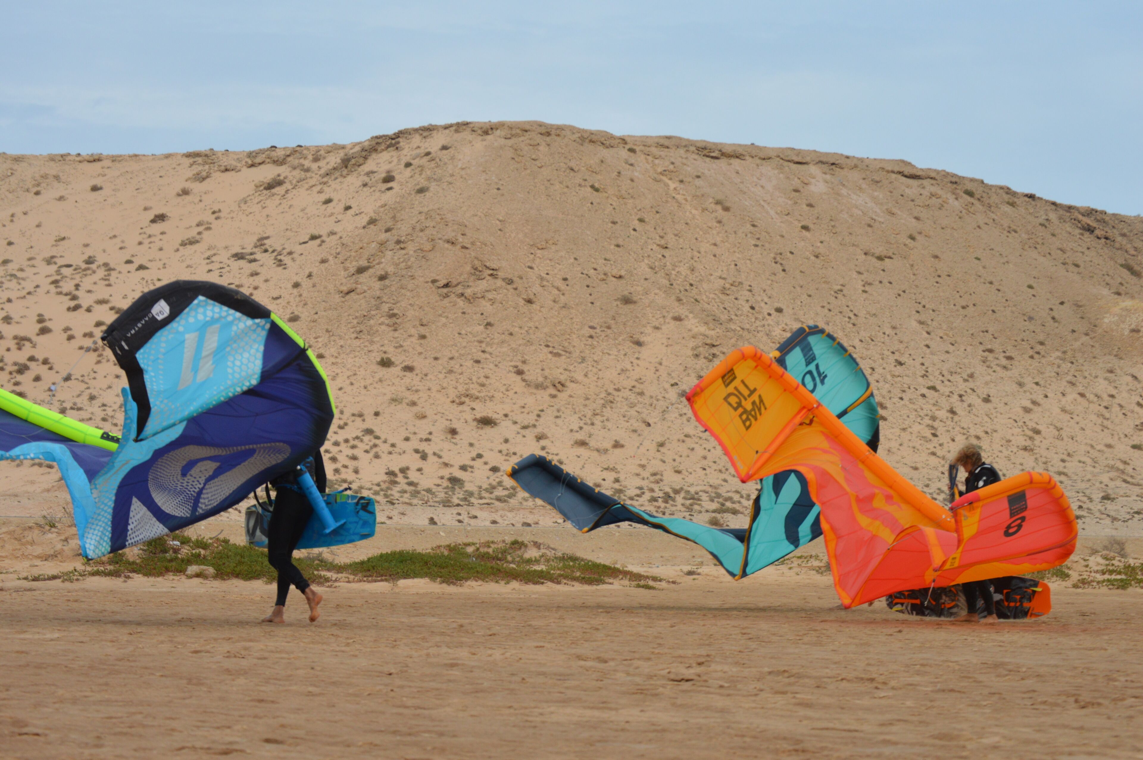 Une plage de sable avec de grands cerfs-volants et une dune en arrière-plan.