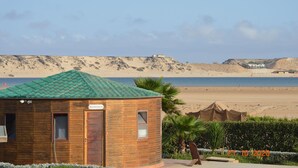 Un edificio de madera con techo verde, un cartel que dice "Maintenance" y una vista de la playa y las dunas al fondo.
