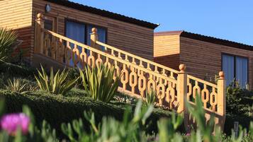 Una casa de madera con una escalera que conduce a la entrada, rodeada de follaje y flores.