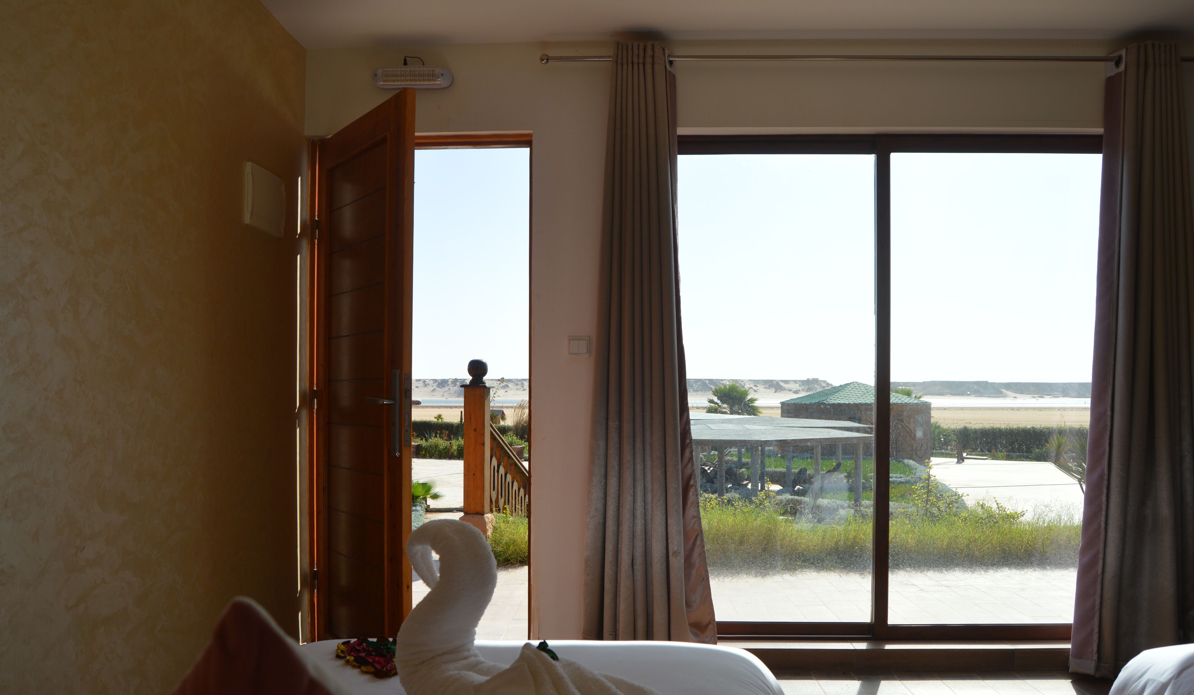 Habitación de hotel con un ventanal grande que ofrece vistas a una playa y un edificio.