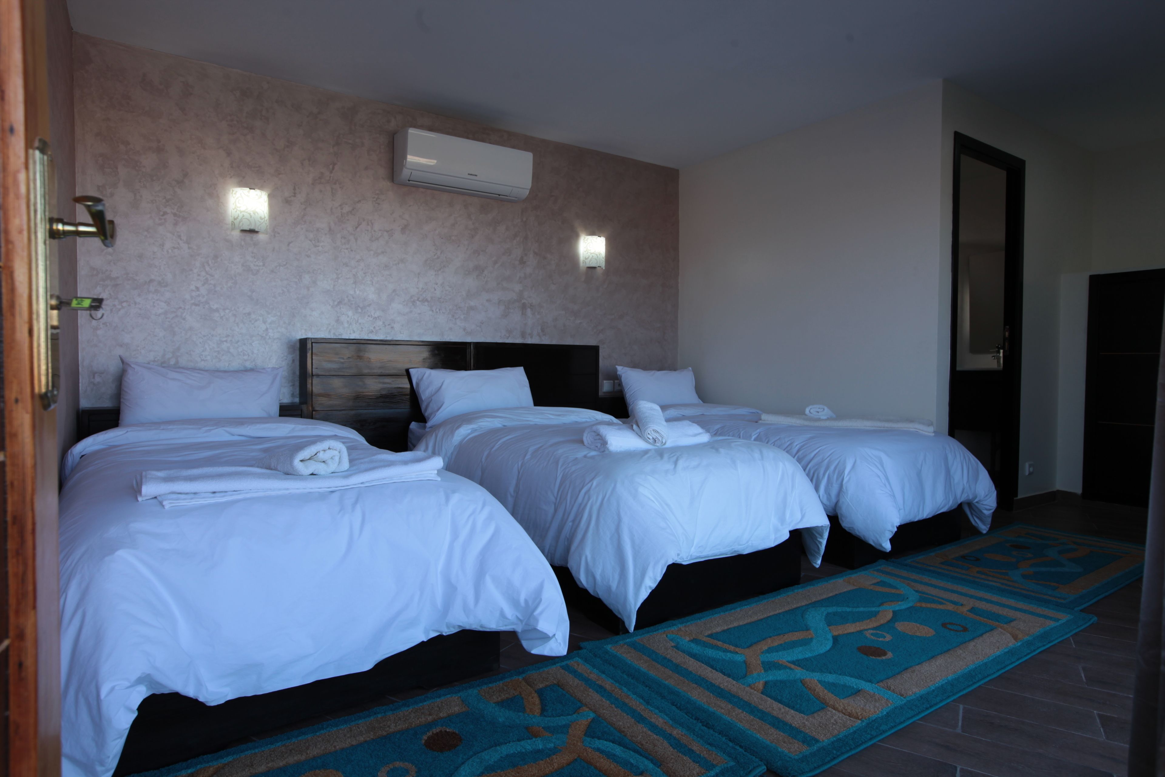 Habitación de hotel con dos camas, cabecero de madera, alfombra estampada y un equipo de aire acondicionado en la pared.