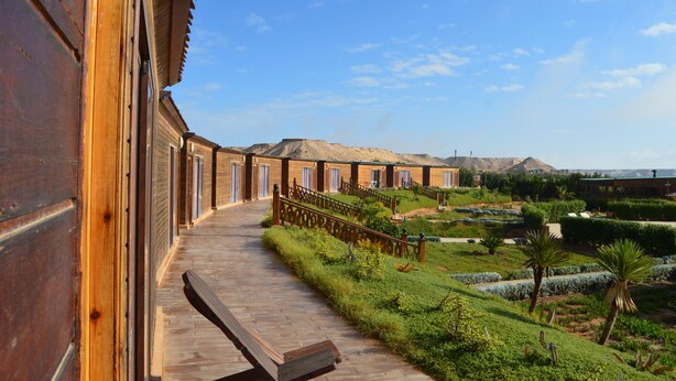 Un pasillo de madera que conduce a varias habitaciones con vistas a un jardín ajardinado y montañas lejanas.