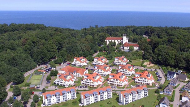 Ett flygbildsbild av ett bostadsområde med flera hyreshus, en tennisbana och en kyrka med ett klocktorn.