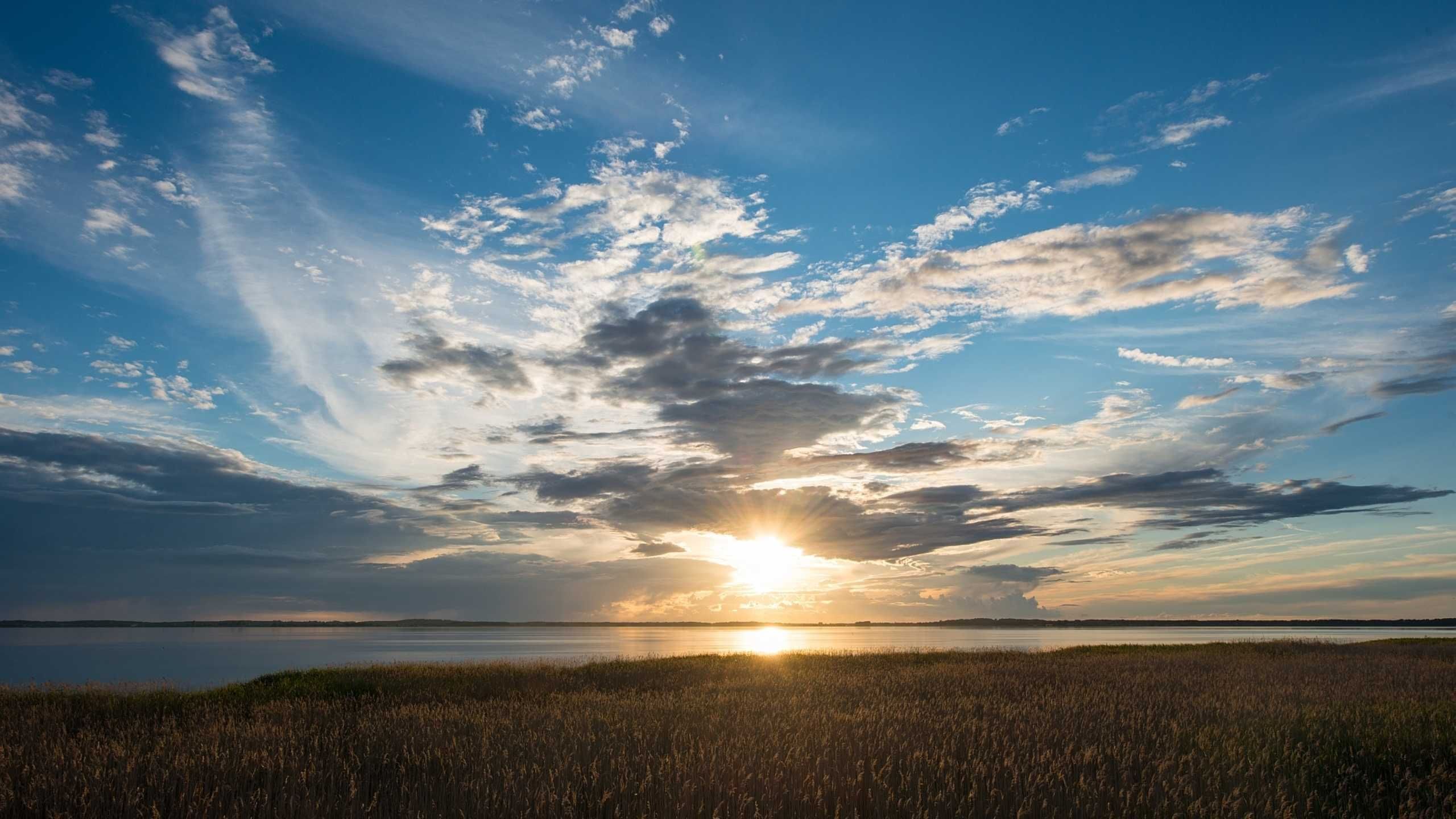 Un coucher de soleil sur une étendue d’eau calme, avec un paysage verdoyant au premier plan.