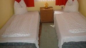 A bedroom with two beds, a nightstand with a lamp, and a window with red curtains. - Holiday house in the old town (Barth)