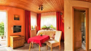 A cozy room with a wooden ceiling, a dining area with a table and chairs, a kitchen with a stove and sink, and a bathroom visible through an open door. - Holiday house in the old town (Barth)