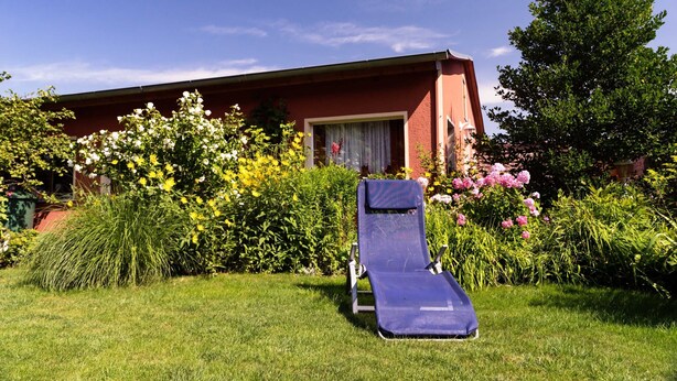 A single-room hotel with a red exterior, a window with a curtain, and a garden with various plants and flowers. - Holiday house in the old town (Barth)