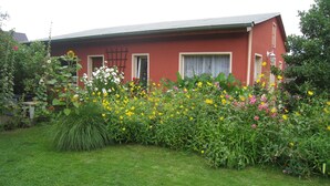 A red building with a sloped roof, surrounded by a well-maintained garden with various flowers and greenery. - Holiday house in the old town (Barth)