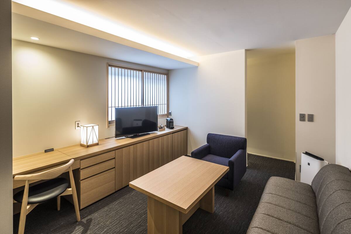Une chambre d’hôtel compacte comprenant un bureau en bois, une télévision, un canapé et une petite table.
