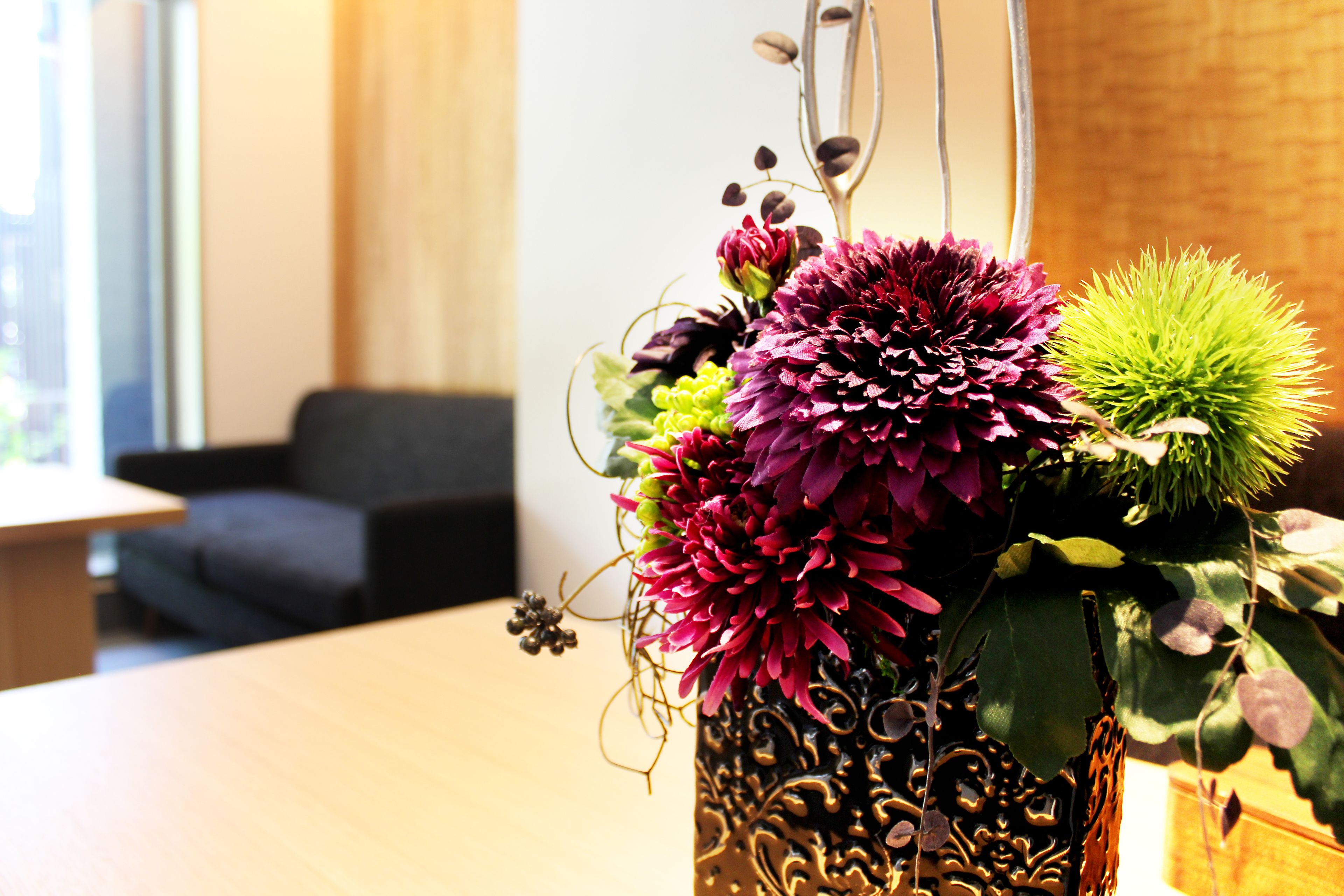 A decorative vase with flowers on a table in a room with a brick wall and a window.