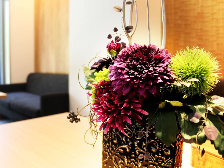 A decorative vase with flowers on a table in a room with a brick wall and a window.
