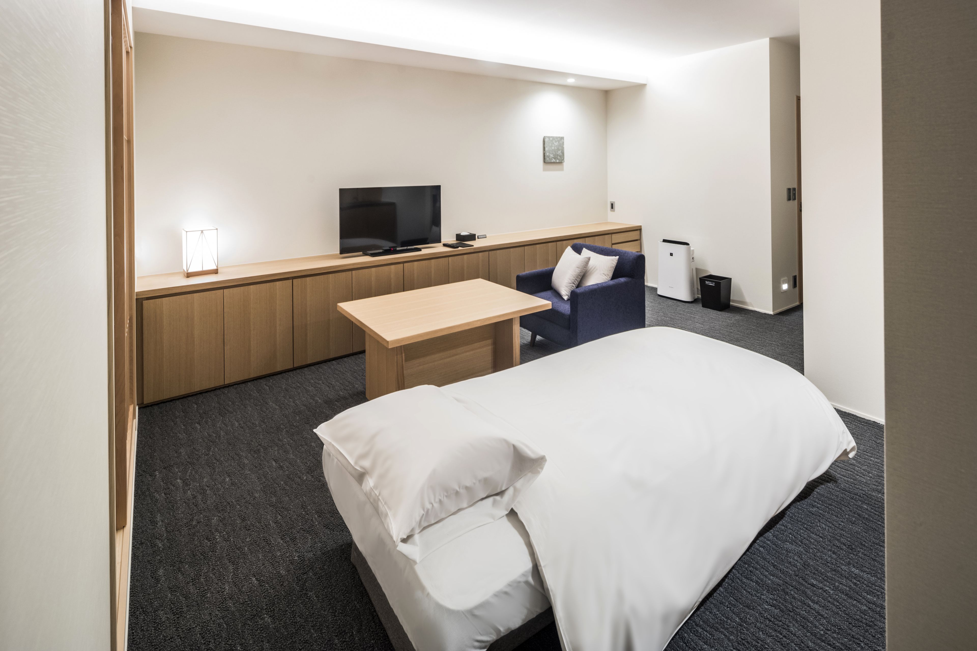 A hotel room with a bed, a desk, a chair, a television, and a small trash bin.