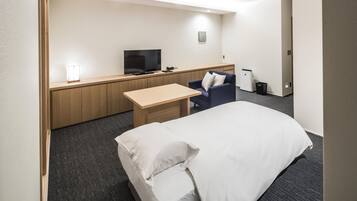 A hotel room with a bed, a desk, a chair, a television, and a small trash bin.