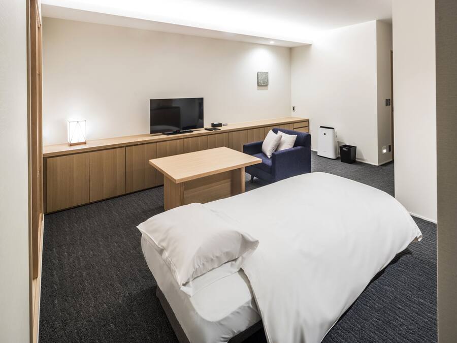 A hotel room with a bed, a desk, a chair, a television, and a small trash bin.